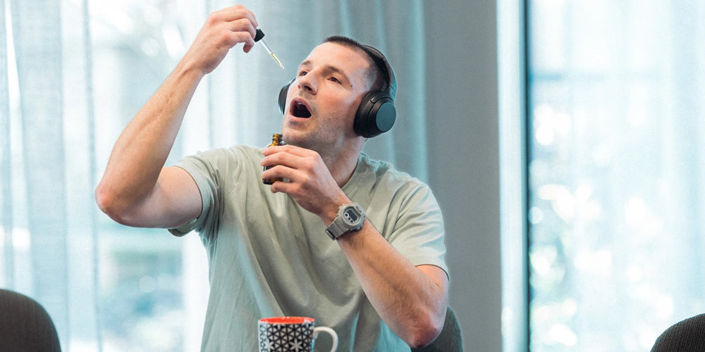 Man with headphones on taking CBD oil drops orally whilst enjoying his morning cup of tea | The CBD Hut