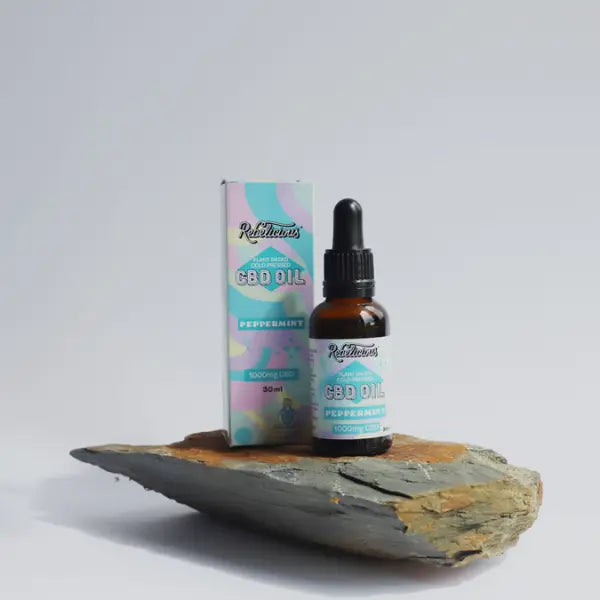 Rebelicious CBD oil bottle and packaging on a stone surface with a light grey background | The CBD Hut