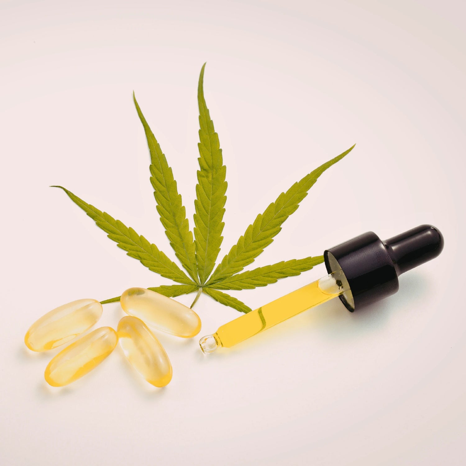 Cannabis leaf, capsules, and dropper with yellow liquid on a light background