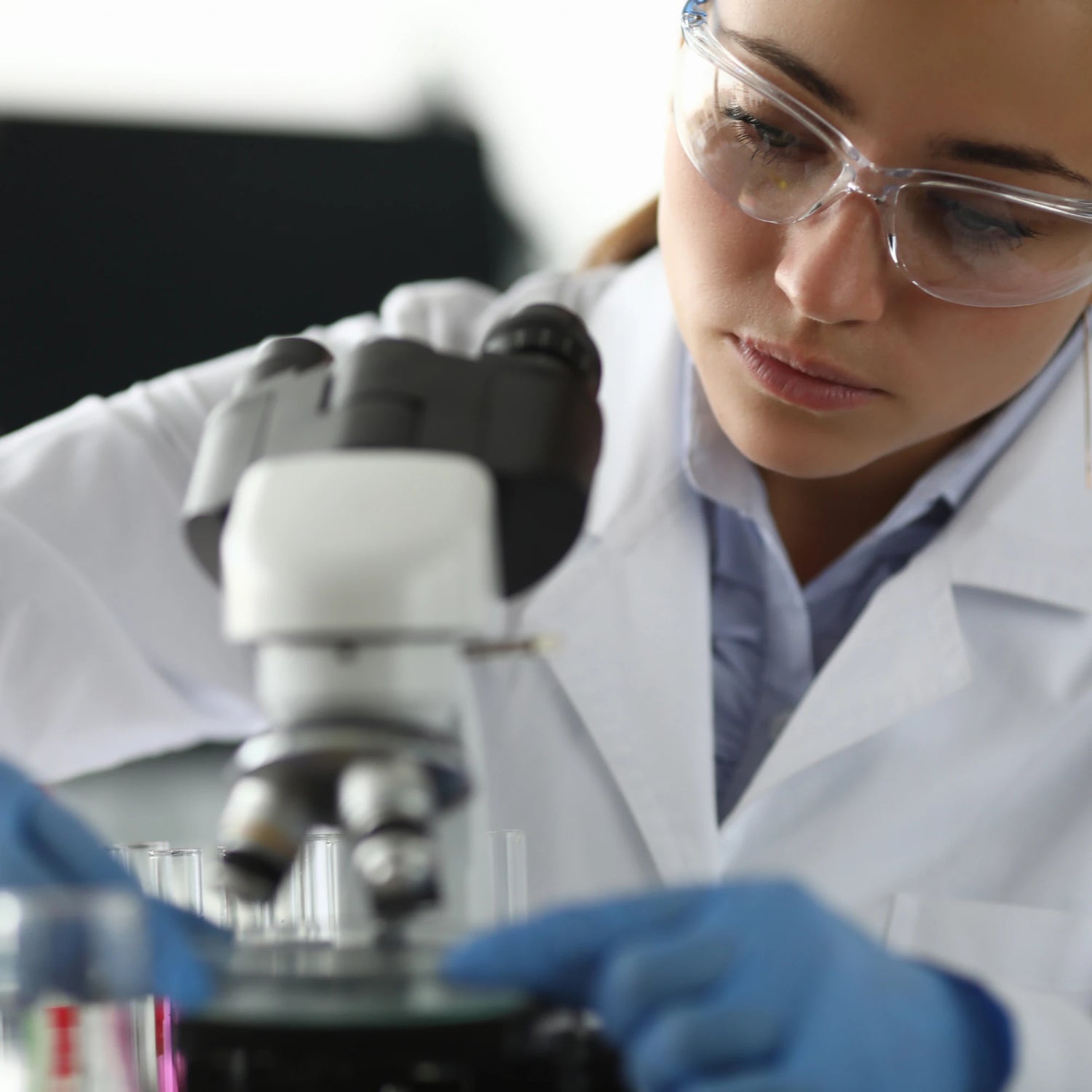 Person wearing goggles and gloves using a microscope to test CBD in a laboratory setting