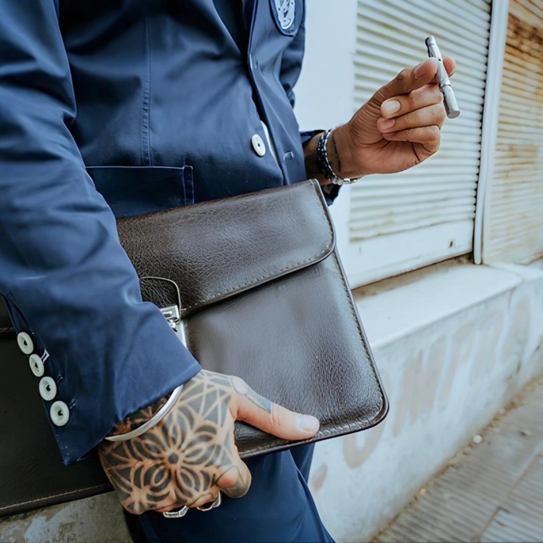 Person holding a brown leather briefcase with a tattooed hand, holding a Dynavap vape pen.