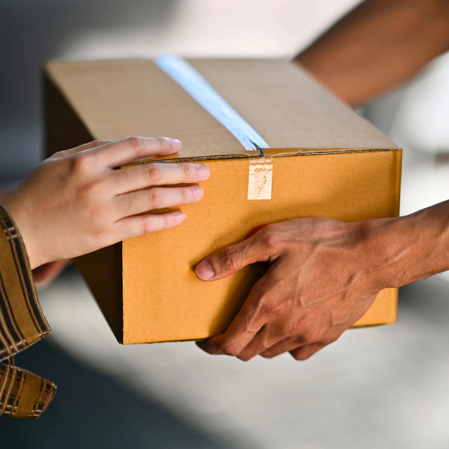 Two hands exchanging a cardboard box with a blurred background