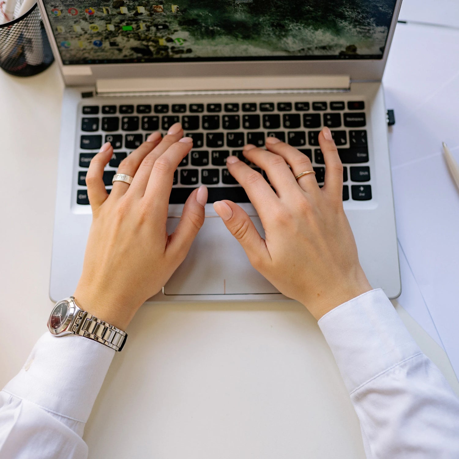 Person typing on a PC on a white table with note pad to the side