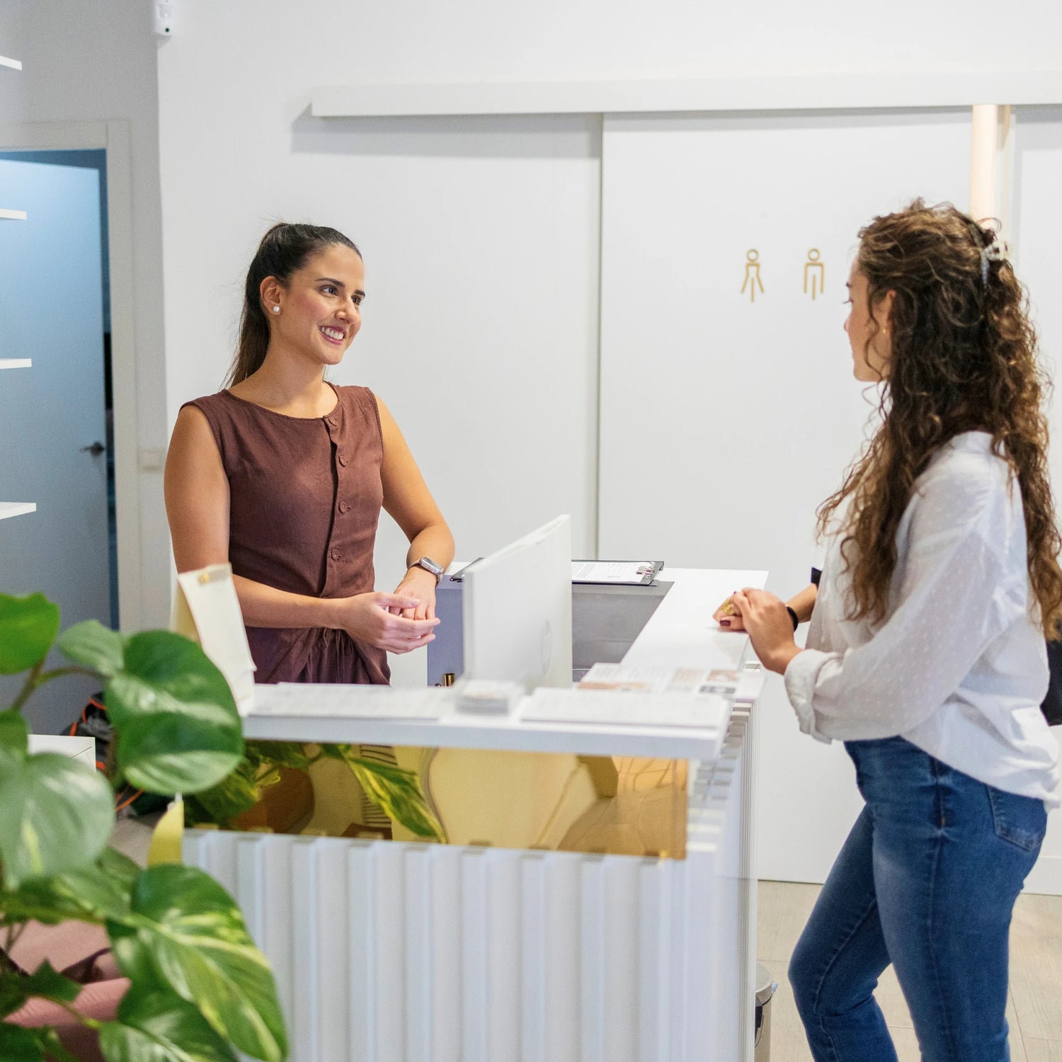 Two women interacting at a reception desk in an office setting.