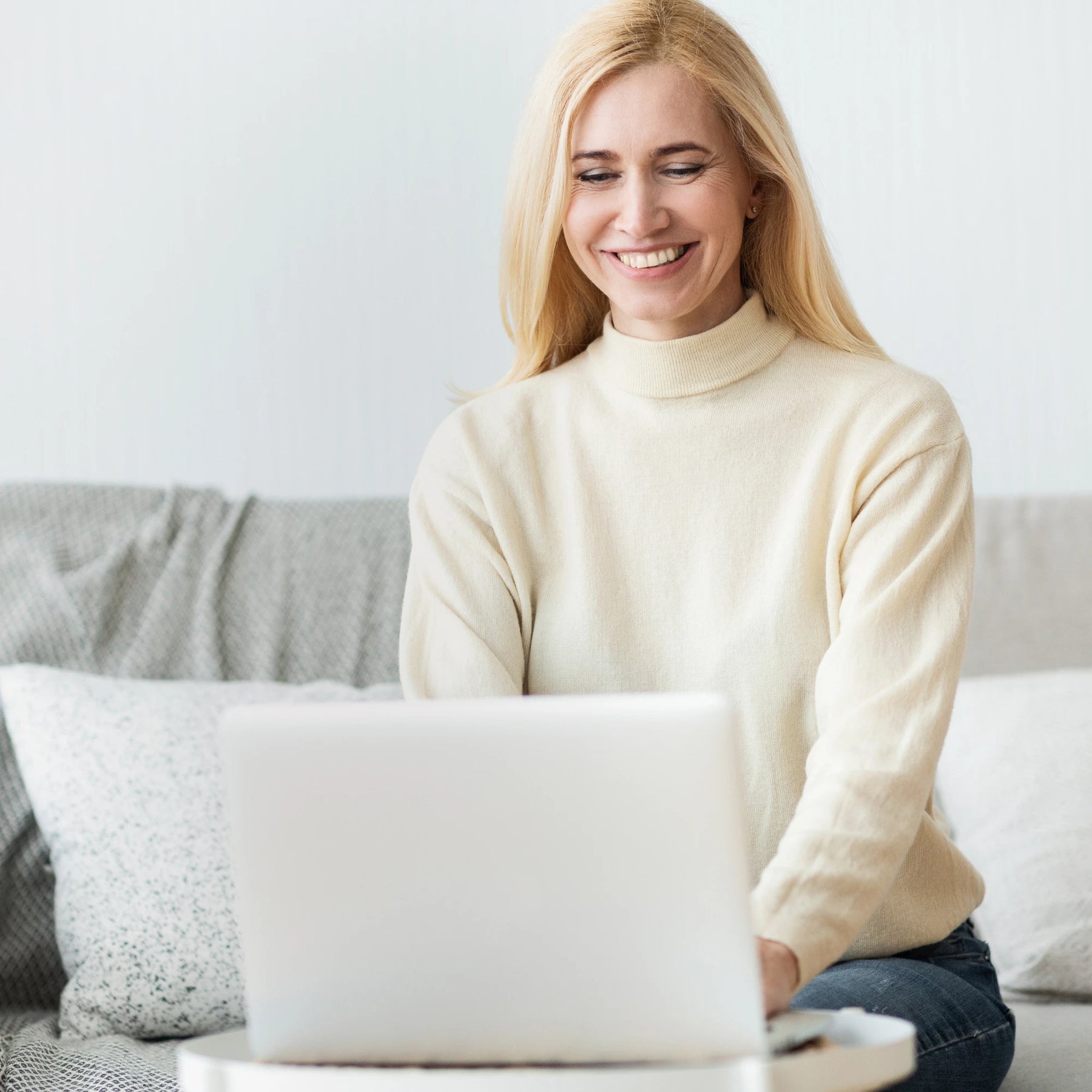 Woman in a cream sweater using a laptop on a couch
