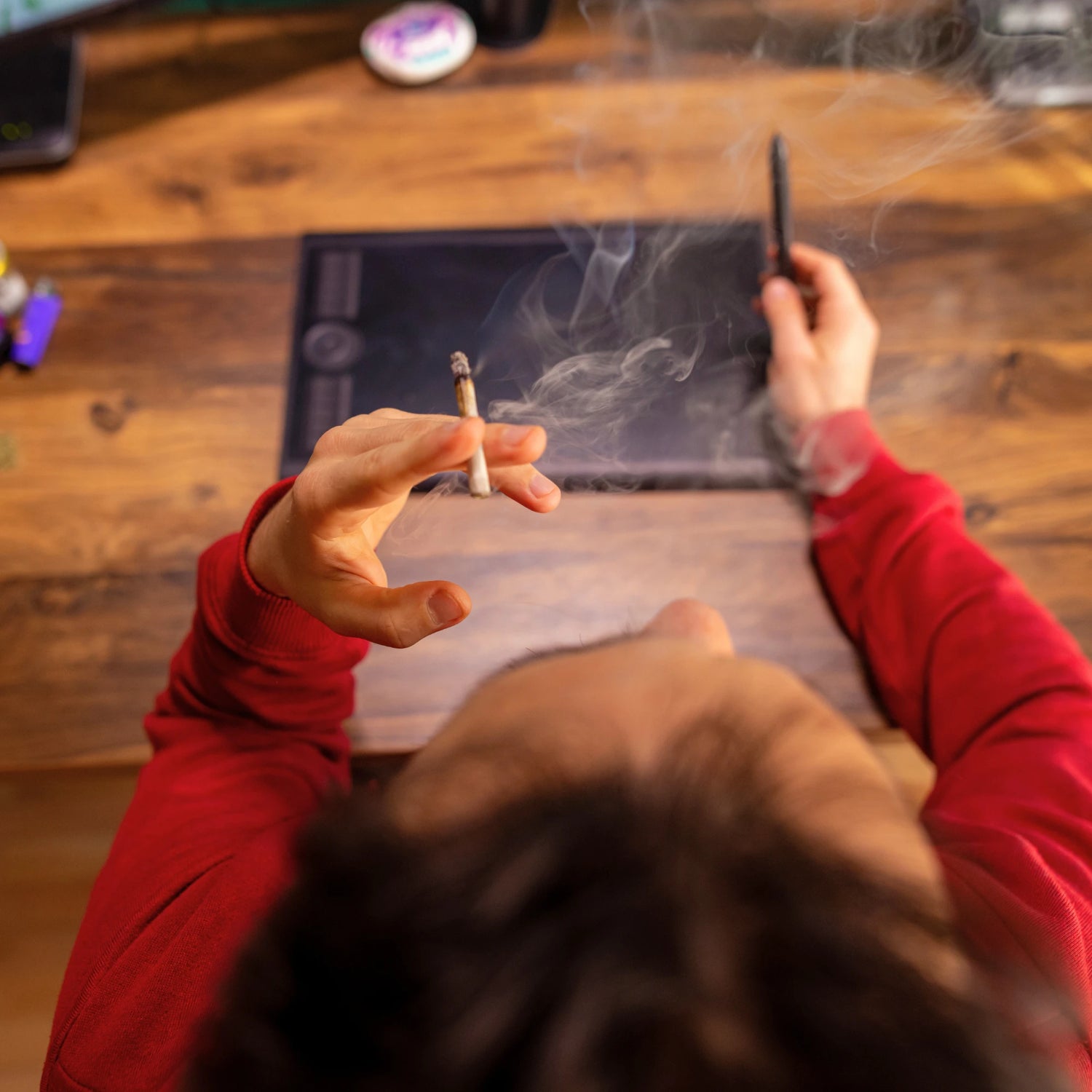 Person smoking a cigarette with a tablet on a wooden table