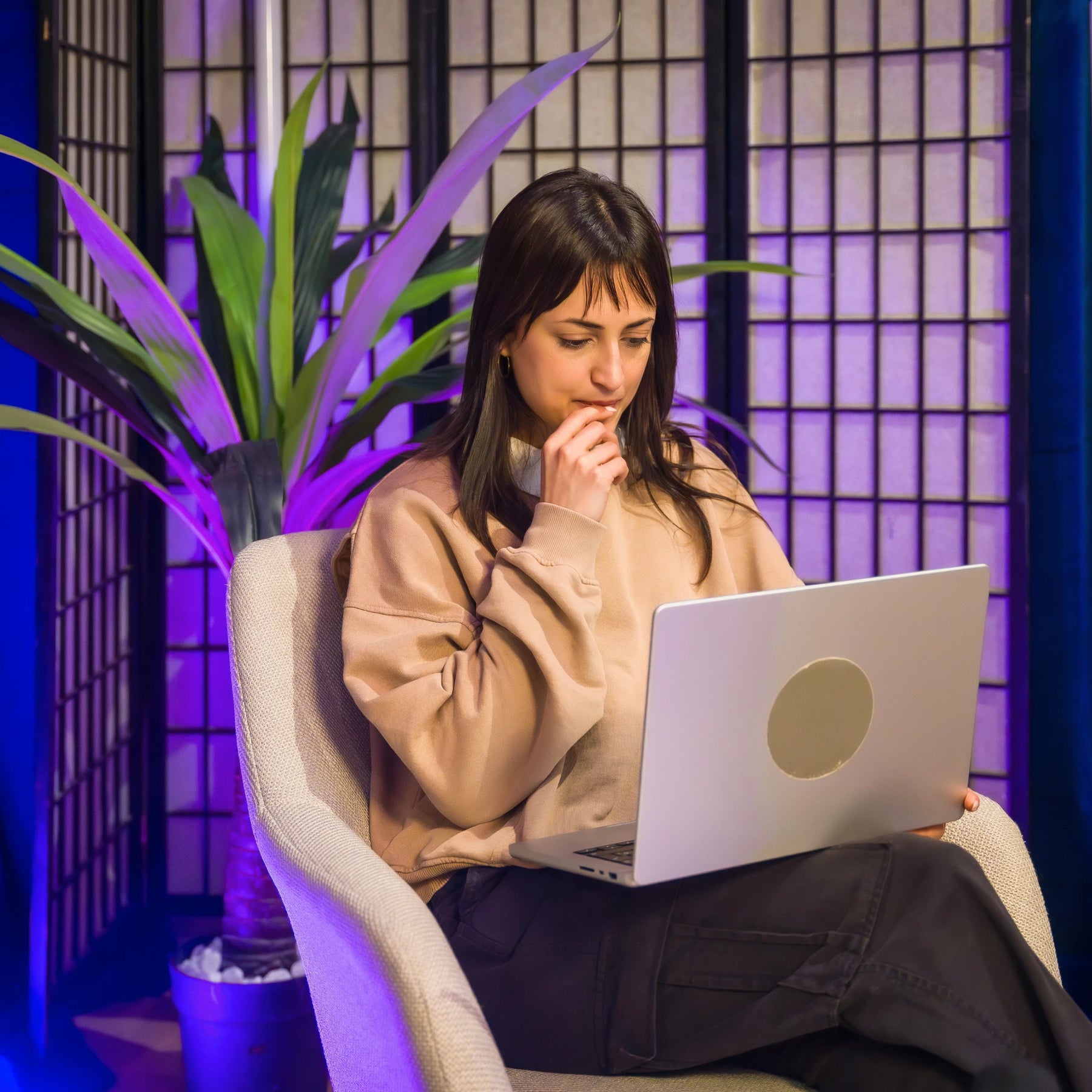Woman using a laptop in a room with purple lighting and plants