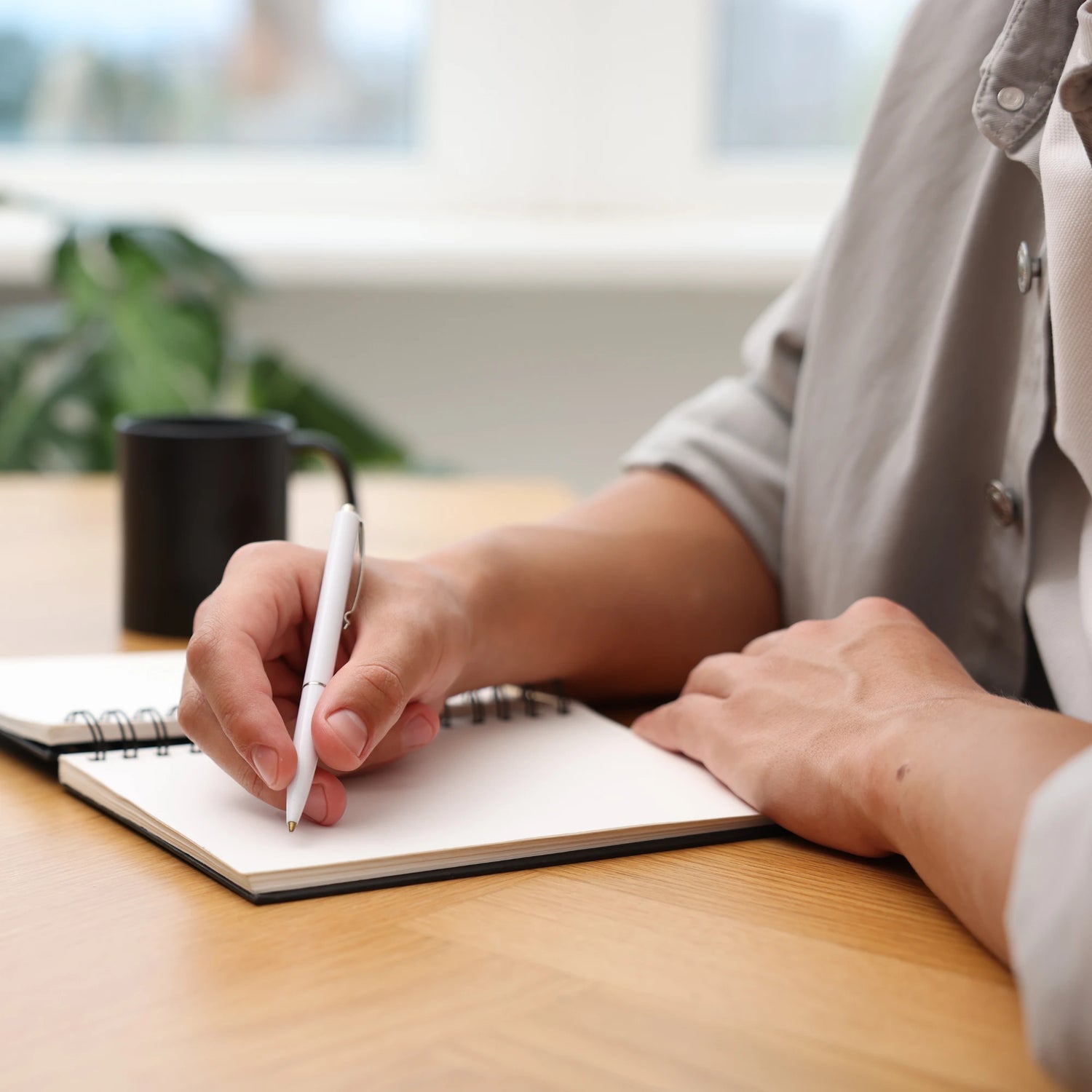 Person writing in notebook on a desk with a homely, lifestyle backdrop