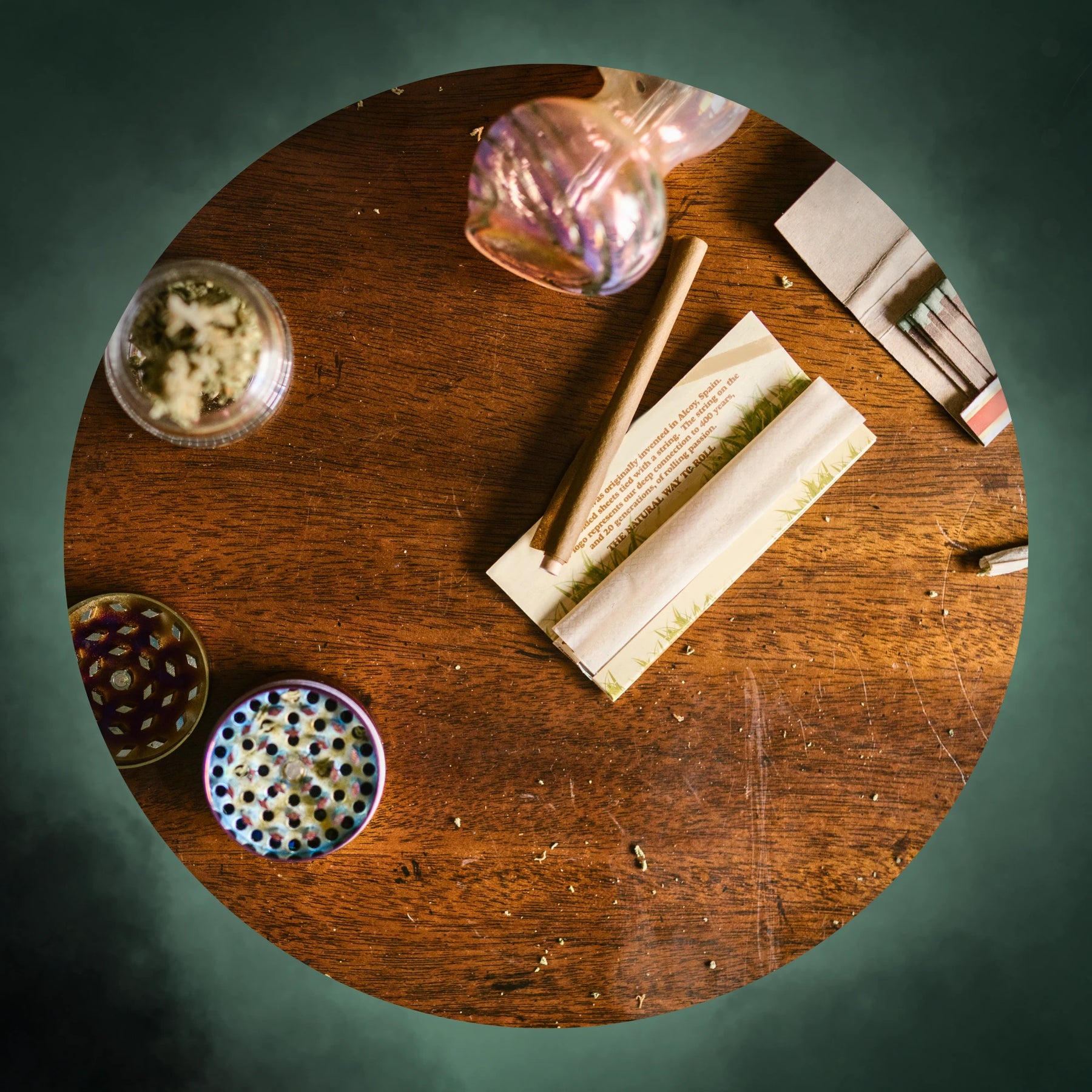 Wooden table with smoking accessories including a glass, rolling paper, and pipes.